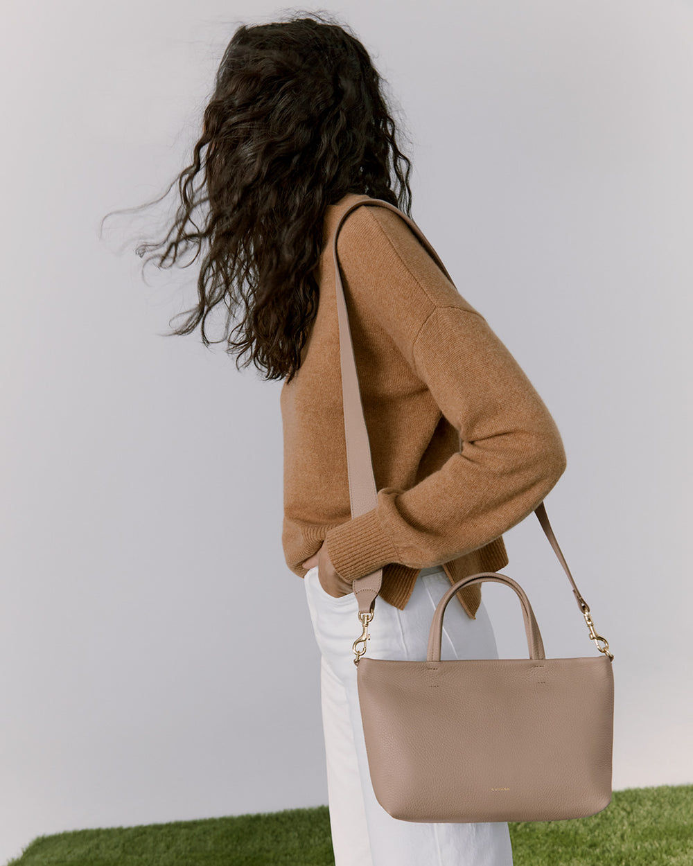 Woman standing with back turned, holding a handbag on her shoulder.