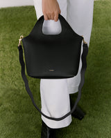 Person holding a handbag with a strap, standing on grass.