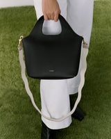 Person holding a handbag while standing on grass.