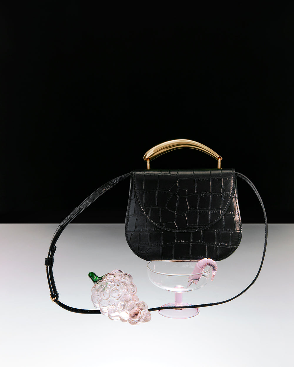 Croc-embossed leather handbag with grapes and glass in foreground.
