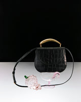 Croc-embossed leather handbag with grapes and glass in foreground.