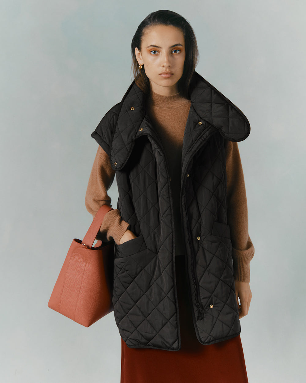 Woman holding a bag, wearing a layered outfit with a quilted vest.
