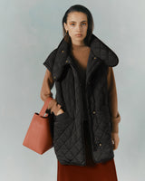 Woman holding a bag, wearing a layered outfit with a quilted vest.