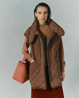 Woman holding a bag and wearing an oversized jacket over a sweater.