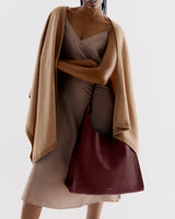 Person in a dress with a cape, holding a large shoulder bag.