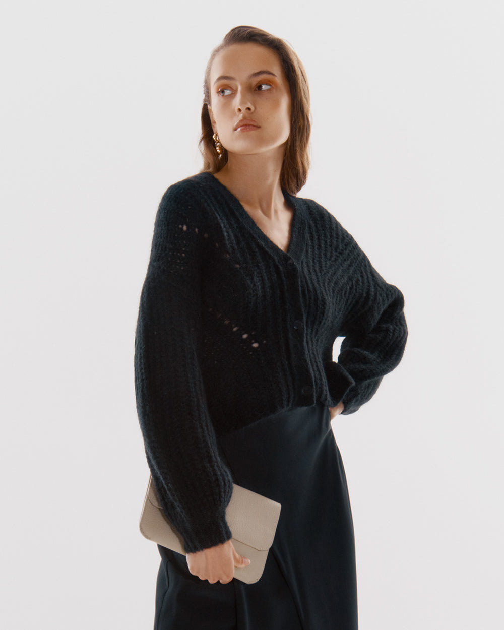 System Flap Bag Woman standing with hand on hip, looking to the side.