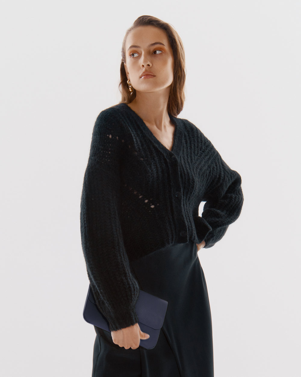 System Flap Bag Person in a cardigan holding a small clutch.