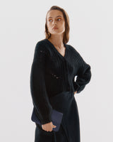 Person in a cardigan holding a small clutch.