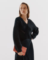 Person in knit sweater holding a small clutch bag.