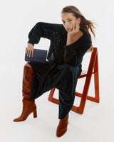 Person seated on a chair wearing a dress and boots, holding a clutch.