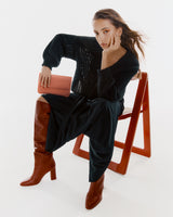 Person sitting on chair with boots and small handbag in hand.