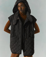 Woman in a hooded vest and long sleeve shirt standing with hands at her sides.