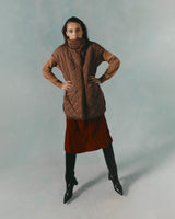 Woman posing with hands on hips, wearing a quilted coat, skirt, and knee-high boots.