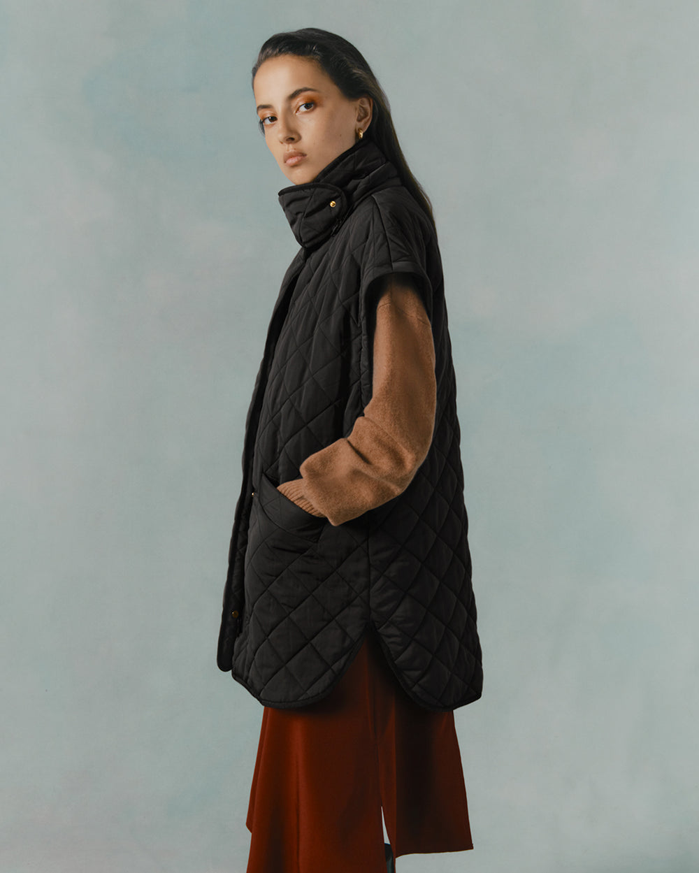 Woman standing in profile wearing a long coat and scarf.