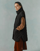 Woman standing in profile wearing a long coat and scarf.