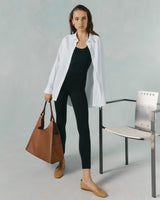 Woman standing by a chair holding a large bag.