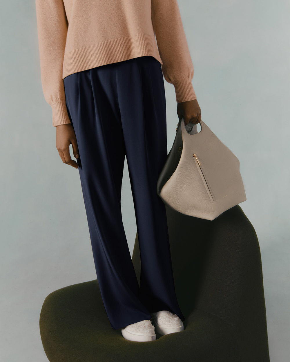 Person standing with a handbag, wearing sneakers and trousers.
