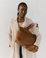 Woman standing and holding a large handbag, wearing a coat.