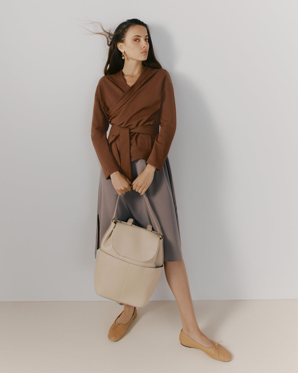 Woman standing holding a handbag, looking sideways.