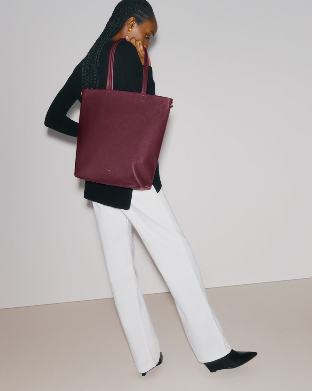 Person holding a tote bag and standing with one leg slightly bent.