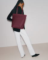 Person holding a tote bag and standing with one leg slightly bent.