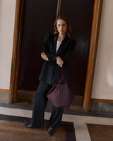 Person in suit holding a large handbag, standing in front of a door.