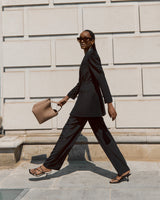 Woman walking by a wall, wearing sunglasses and holding a bag.
