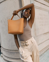 Woman posing with a handbag near a stone structure.