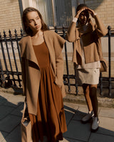 Two women standing by a fence, one shading her eyes, both dressed in coats.