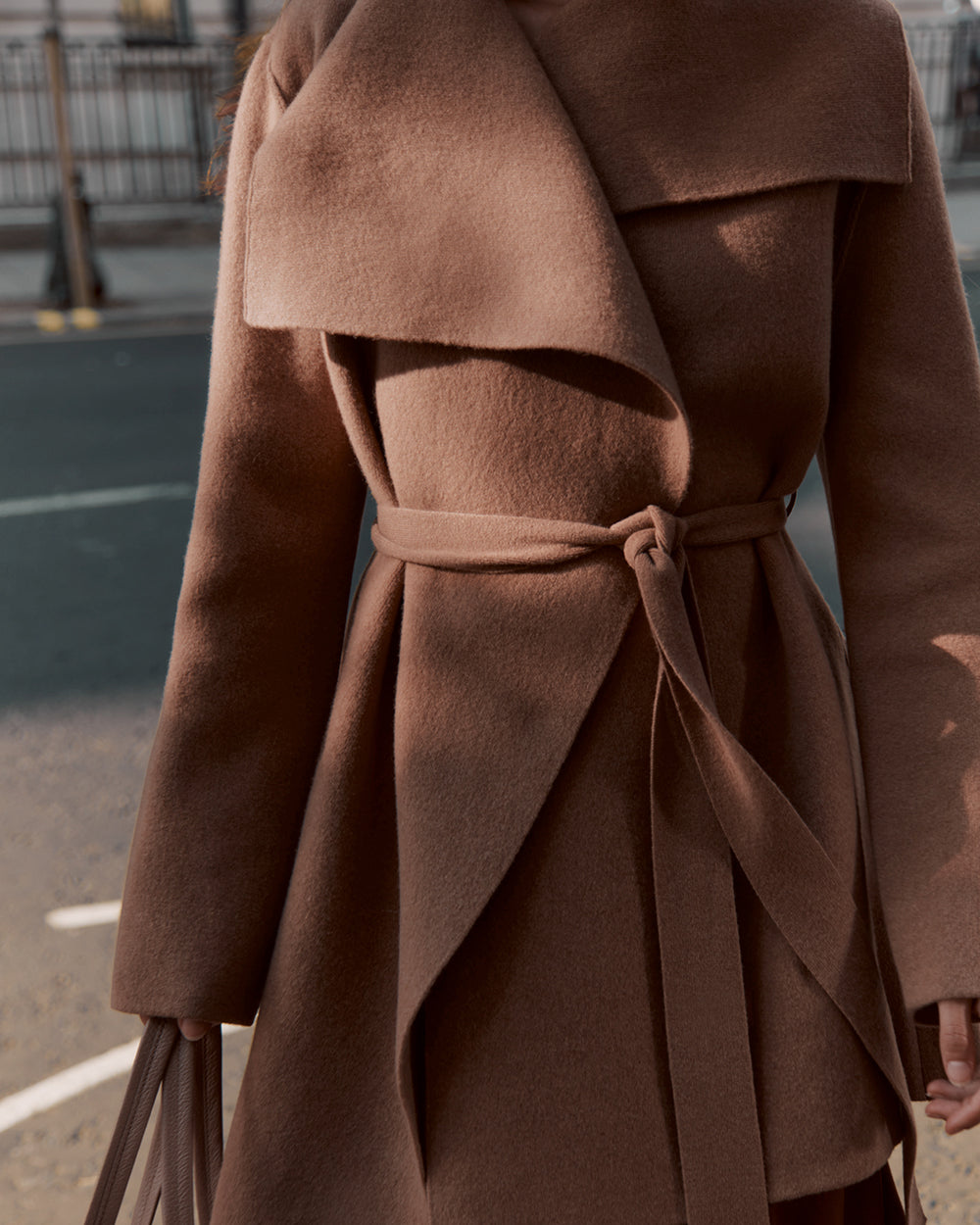Person wearing a belted sweater and carrying a bag in an urban setting