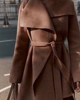 Person wearing a belted sweater and carrying a bag in an urban setting