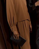 Person holding a clutch bag, wearing a pleated dress and standing next to another person.