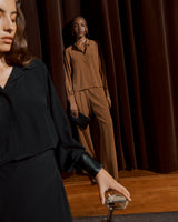 Two women standing by a curtain, one in the foreground partially shown.