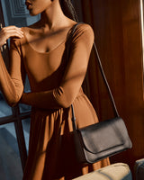 Woman in a dress with a shoulder bag standing by a door.