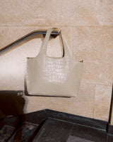 Handbag hanging on a railing against a tiled wall background.