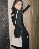 Woman leaning against a wall with a handbag over her shoulder.