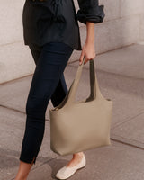 Person holding a large handbag while walking on a sidewalk.