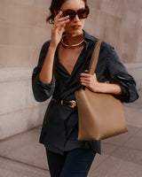 Person wearing sunglasses and holding a structured handbag, walking outdoors.
