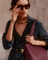 Person wearing sunglasses, a necklace, and holding a large bag on their shoulder.