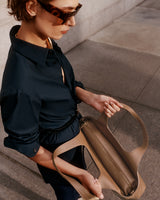 Person holding an open handbag and looking inside while standing outside.