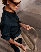 Person wearing sunglasses holding an open handbag with both hands on a city sidewalk.