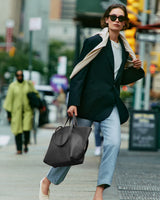 Person walks on city street holding a handbag with a cape draped over shoulders.