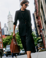 Person in a blazer and skirt walking on a city street, carrying a large handbag
