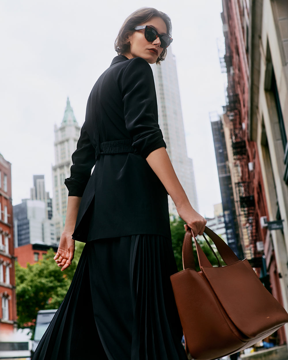 Person in black walking on a city street carrying a travel bag.