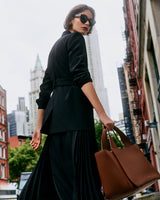 Person in black walking on a city street carrying a travel bag.