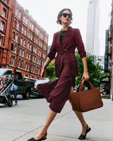 Person walking in city wearing a red blazer and skirt and carrying a large bag