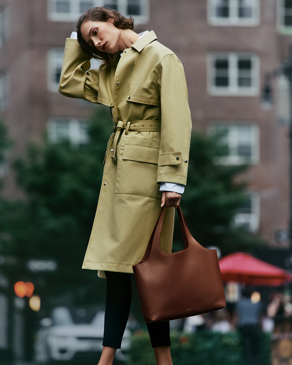 System Tote 13-inch Person wearing a trench coat holding a large tote bag standing on a city street.