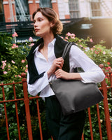 Person holding bag, standing near a fence with flowers in the background.