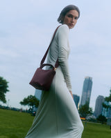 Person in long dress walking in park with shoulder bag and city skyline in background