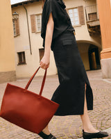 Person walking with large bag through courtyard with rustic buildings in background.